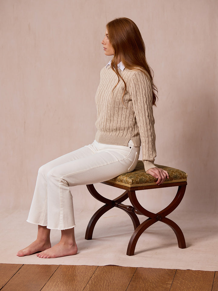 A woman modeling the Malt pink cable-knit sweater sat on a stool