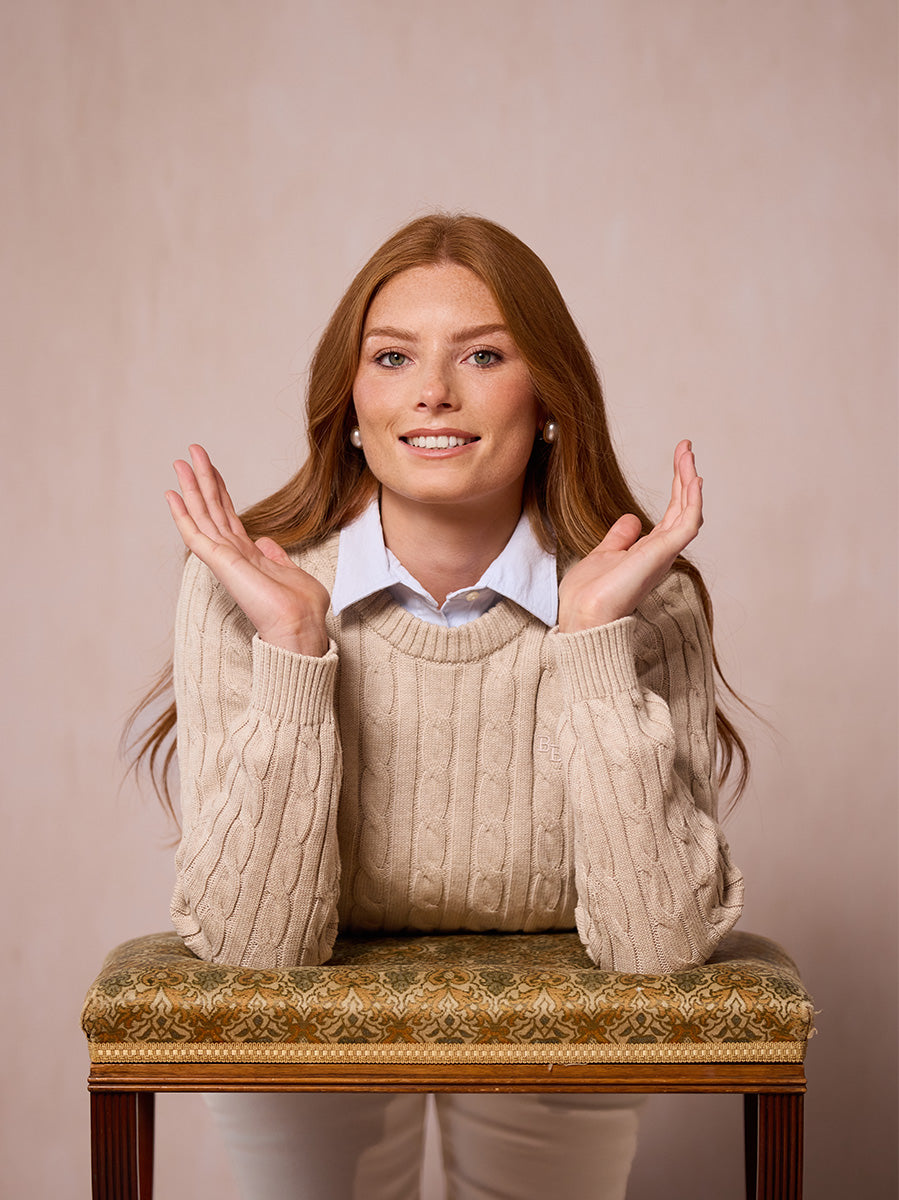 A woman modeling the Malt pink cable-knit sweater leant on a stool