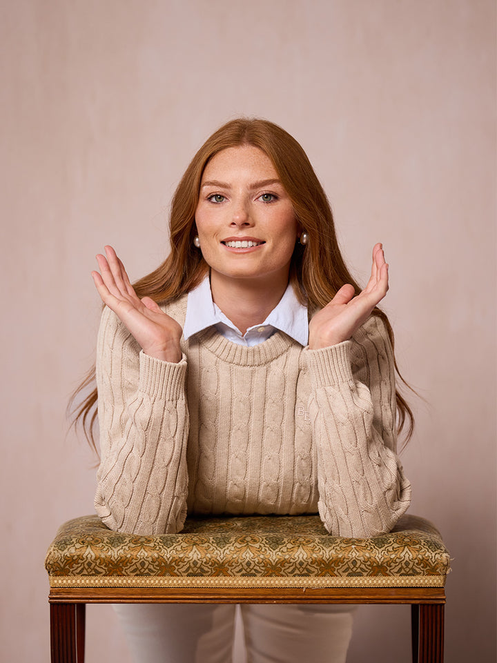 A woman modeling the Malt pink cable-knit sweater leant on a stool