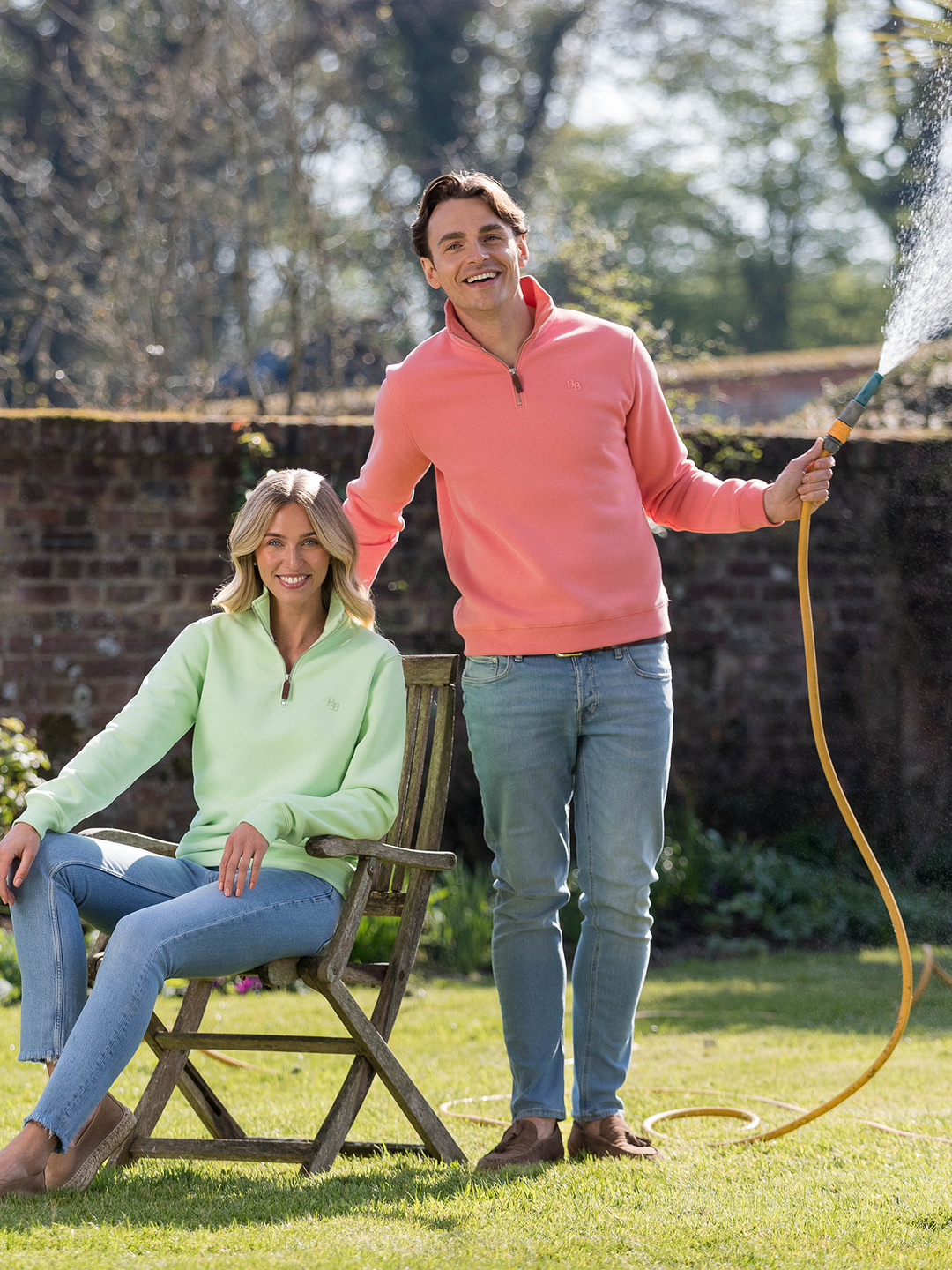 Man wearing a flamingo (coral) pink quarter-zip pullover sweatshirt with subtle embroidered logo, styled casually with light blue jeans.