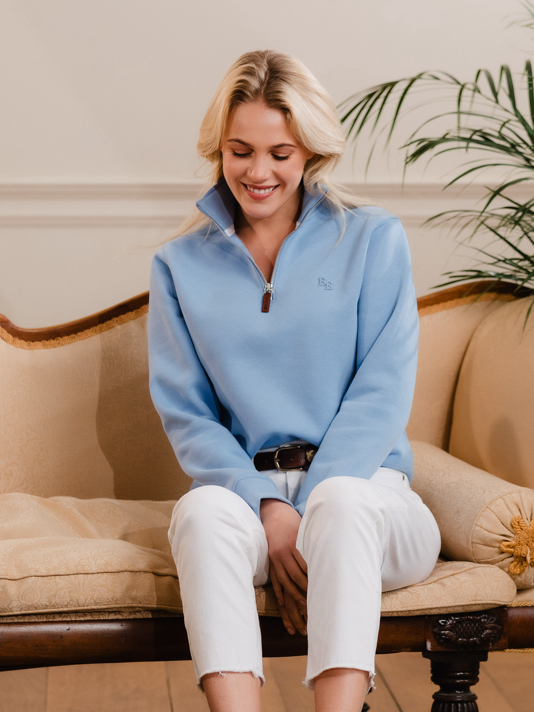 Women wearing a cornflower blue (light blue) quarter-zip pullover sweatshirt with subtle embroidered logo, styled casually with white jeans.